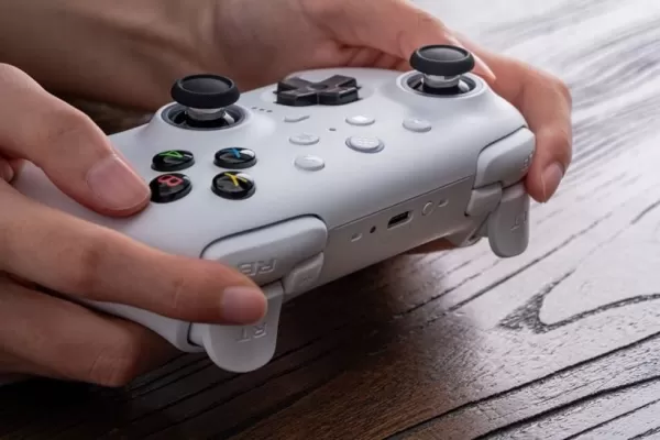 Isang larawan ng isang tao na may hawak na isang puting controller ng laro sa isang kahoy na desk